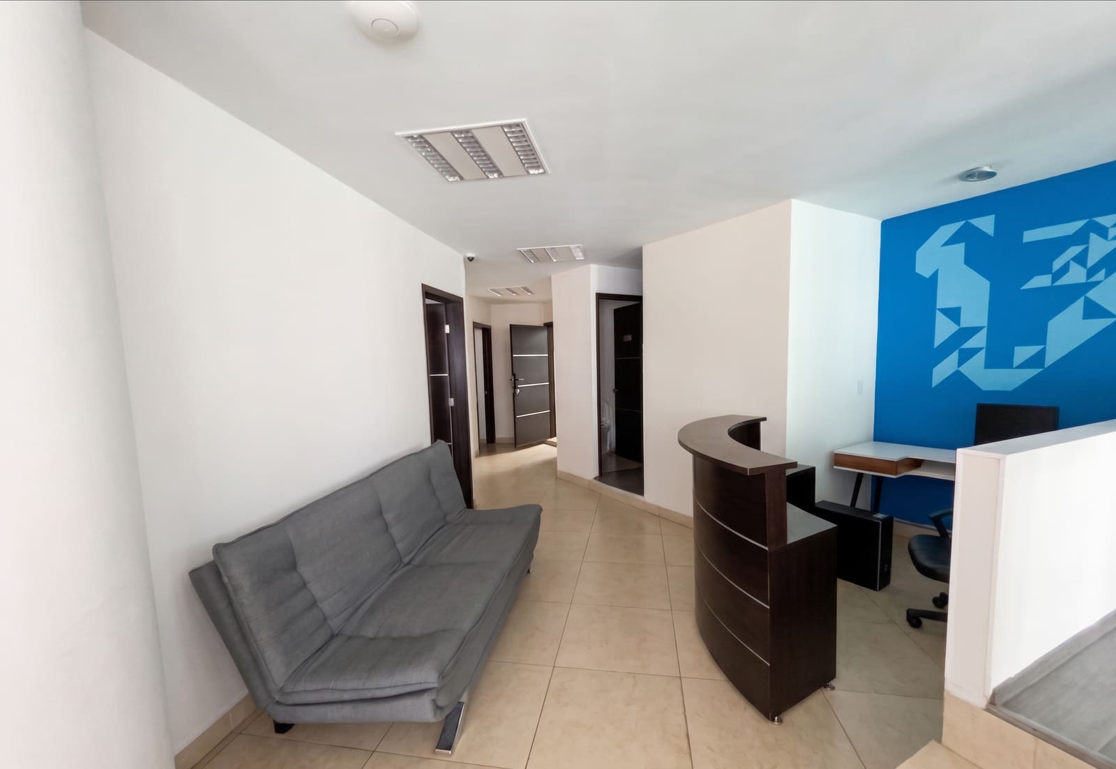 Recepción y lounge de la oficina de 148 m² con sofá y mostrador de madera oscura