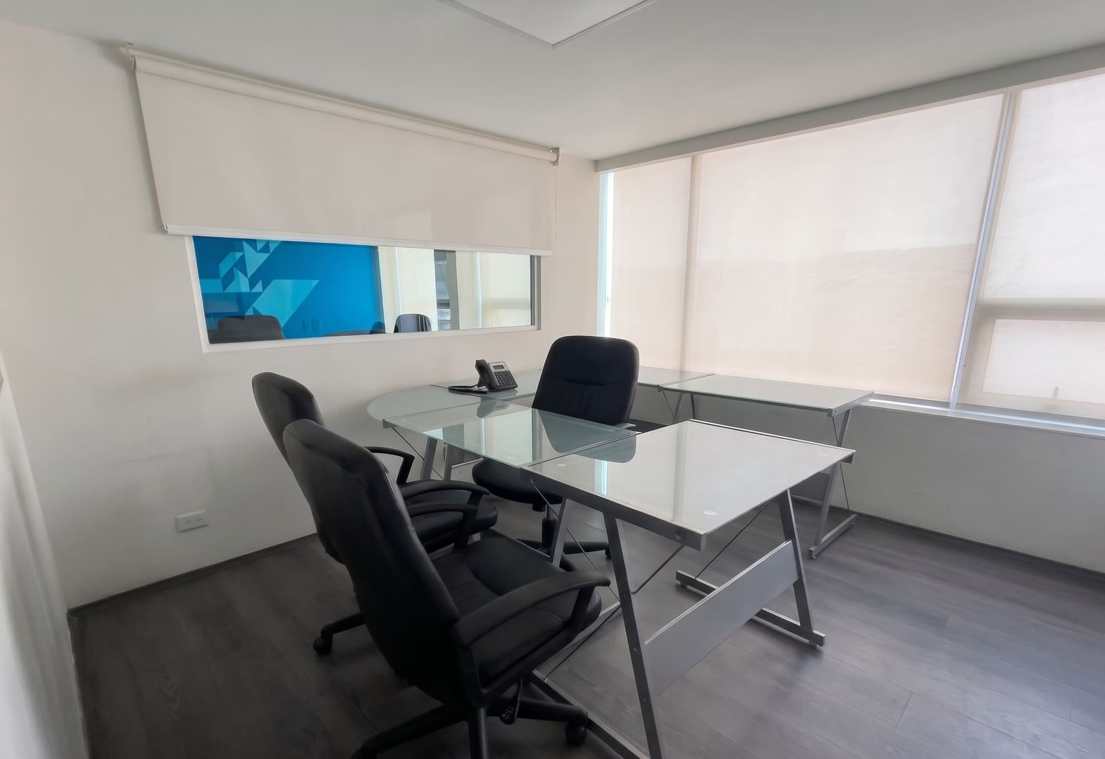 Oficina privada con escritorio en L y luz natural a través de cortinas
