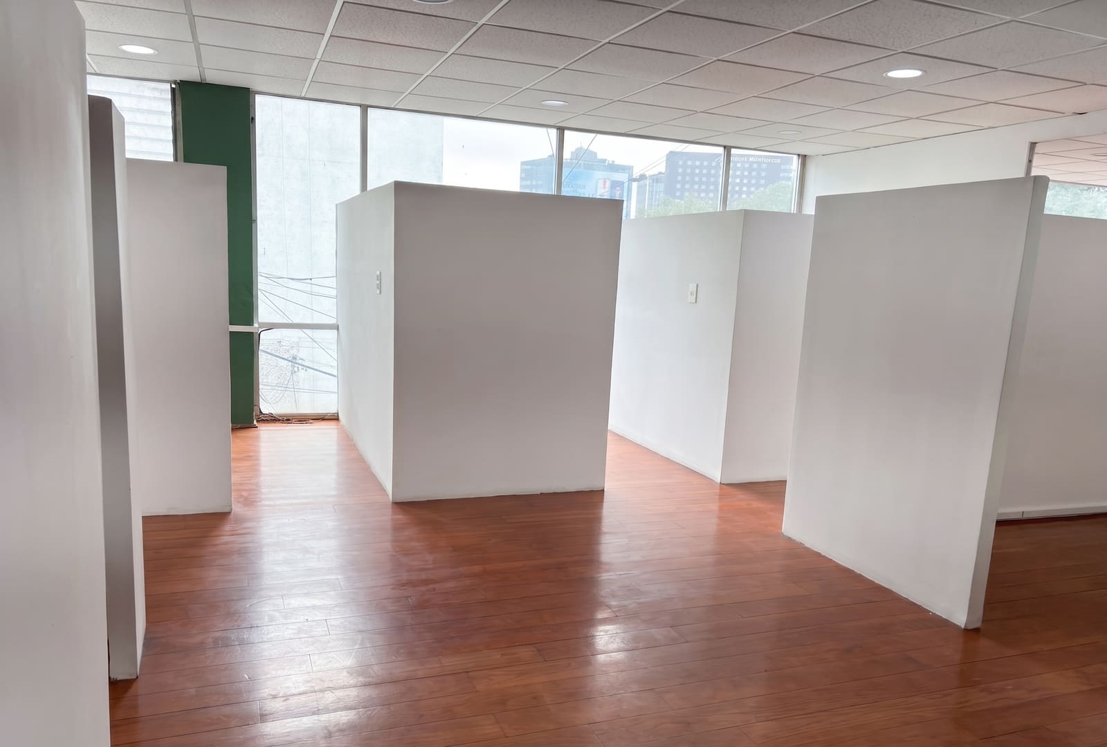 Vista panorámica de la oficina de 150 m² con divisiones de tablaroca blancas tipo cubículo y ventanal al exterior