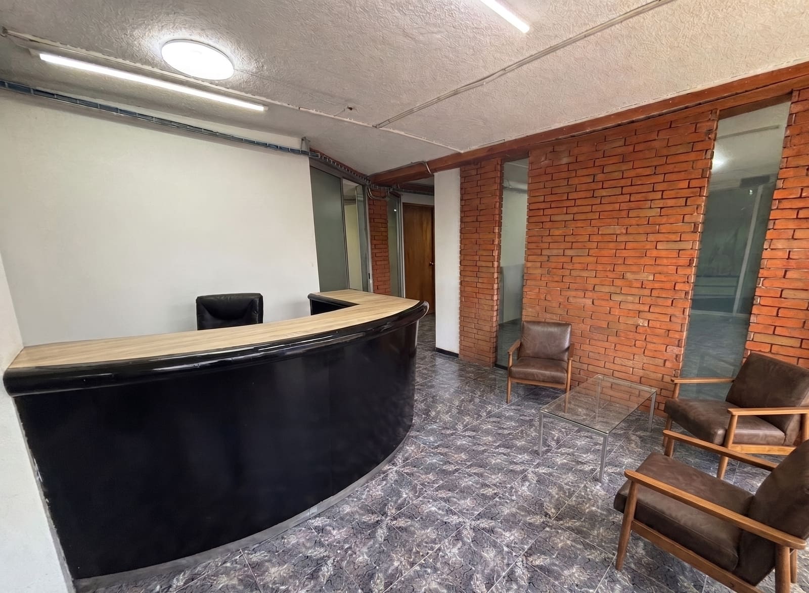 Recepción de la oficina de 450 m² con muro de ladrillo y mostrador de madera oscura