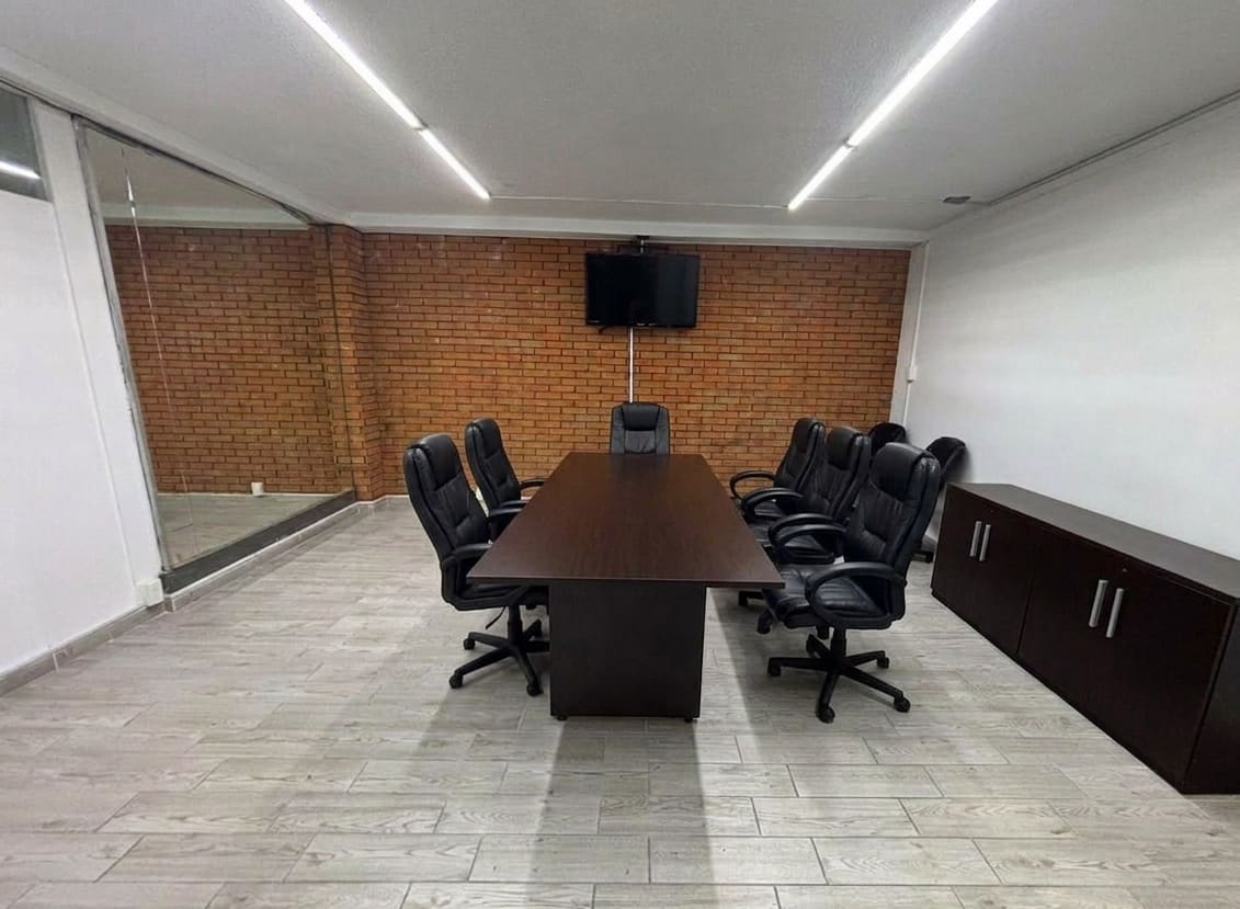 Sala de juntas grande con mesa rectangular, sillas ejecutivas y pantalla